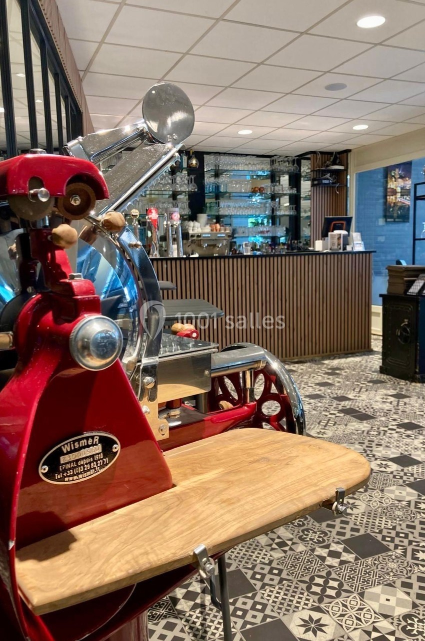 Trancheuse rouge vintage en premier plan, avec un bar moderne et des étagères de verres en arrière-plan.