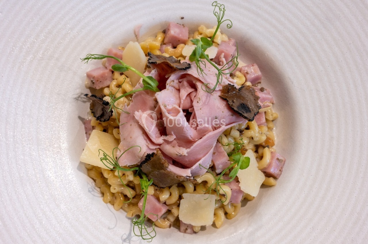 Assiette de pâtes garnie de jambon, truffes, copeaux de fromage et herbes fraîches.