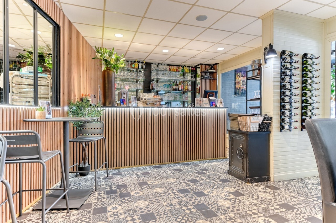Comptoir de bar moderne avec revêtement en bois, étagères de bouteilles, tables hautes et sol en carreaux décoratifs.