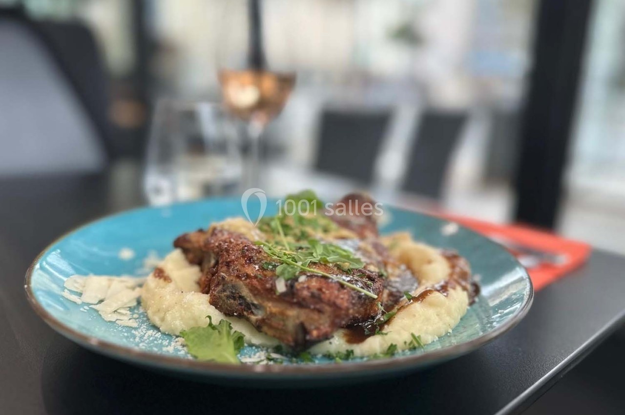 Assiette de poulet grillé sur purée, garnie de verdure et de copeaux de fromage, servie sur une table de restaurant.