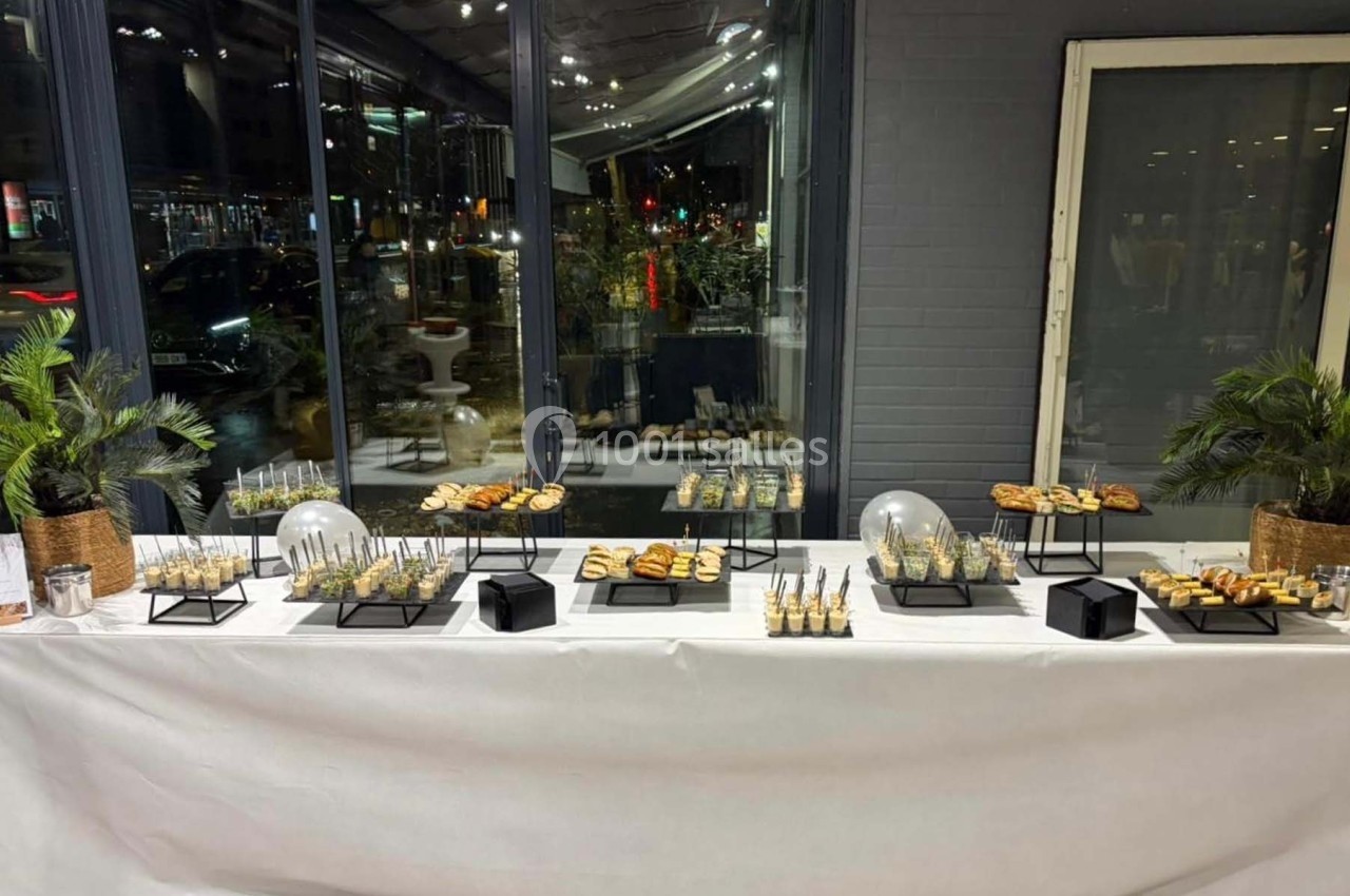 Buffet de réception avec verrines, amuse-bouches et décorations végétales sur une table blanche devant une baie vitrée.