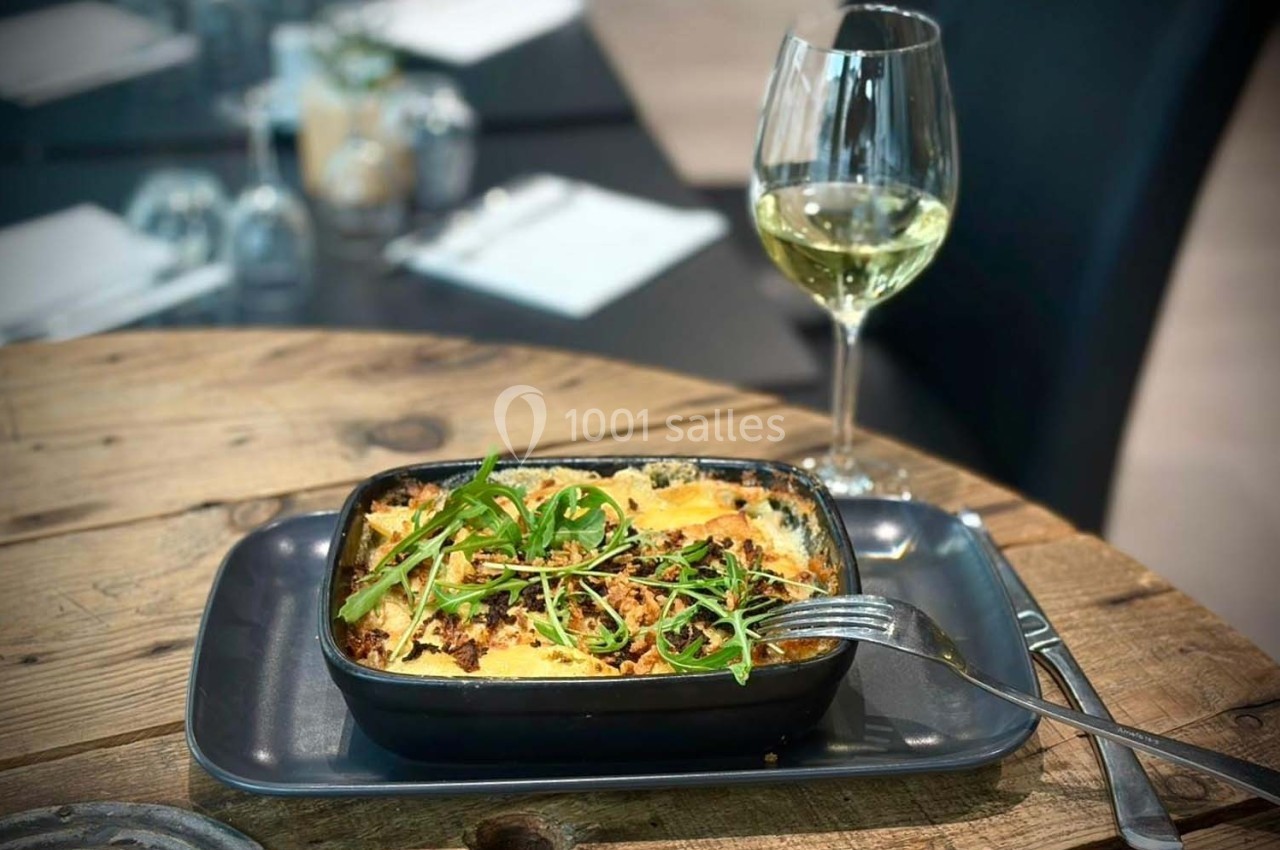 Plat de gratin garni de roquette sur une table en bois, accompagné d'un verre de vin blanc.