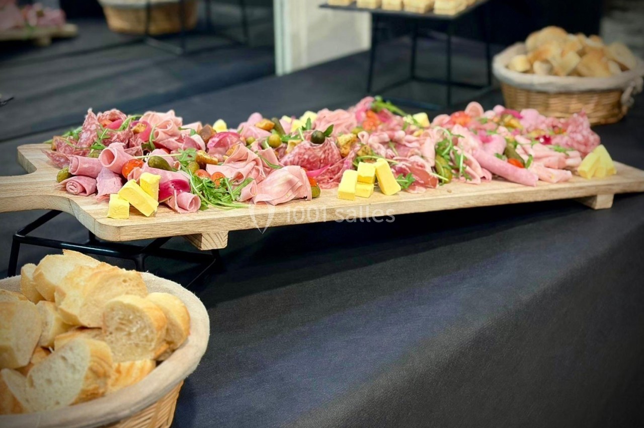 Plateau de charcuterie variée avec fromages, salade et pain en paniers sur une table recouverte d'une nappe noire.