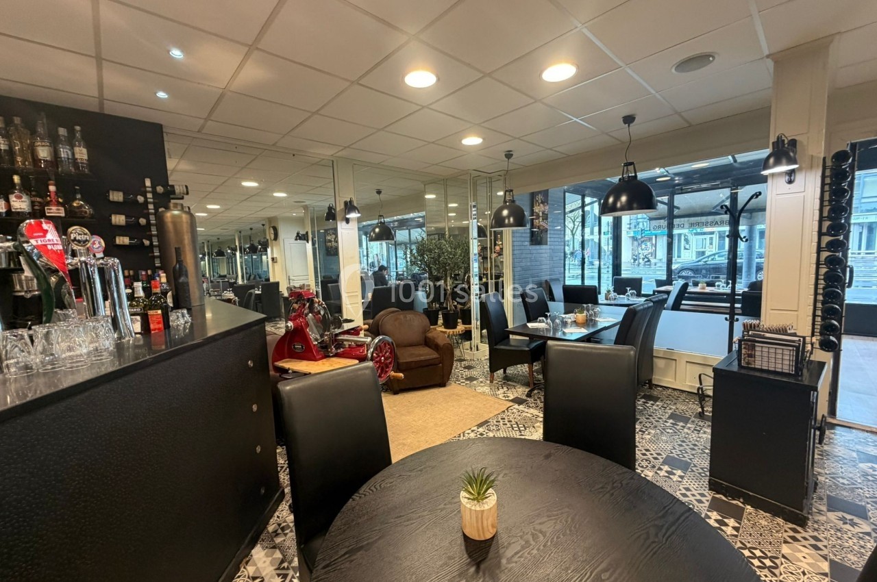 Intérieur d'un restaurant avec mobilier moderne, comptoir de bar, tables noires et sol en carrelage décoratif.
