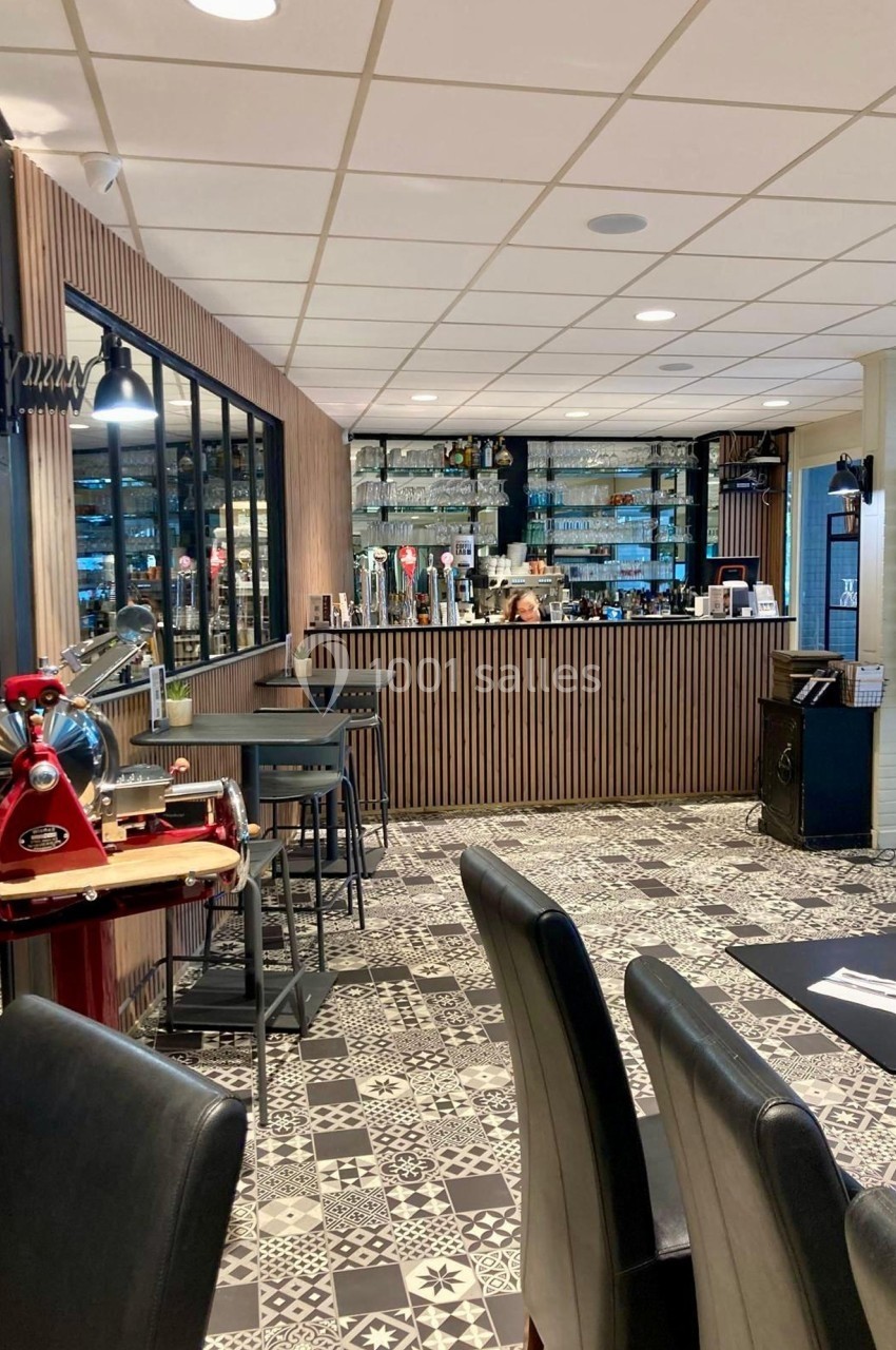 Salle de restaurant avec un bar en bois, des tables dressées, un sol à motifs et une trancheuse rouge au premier plan.