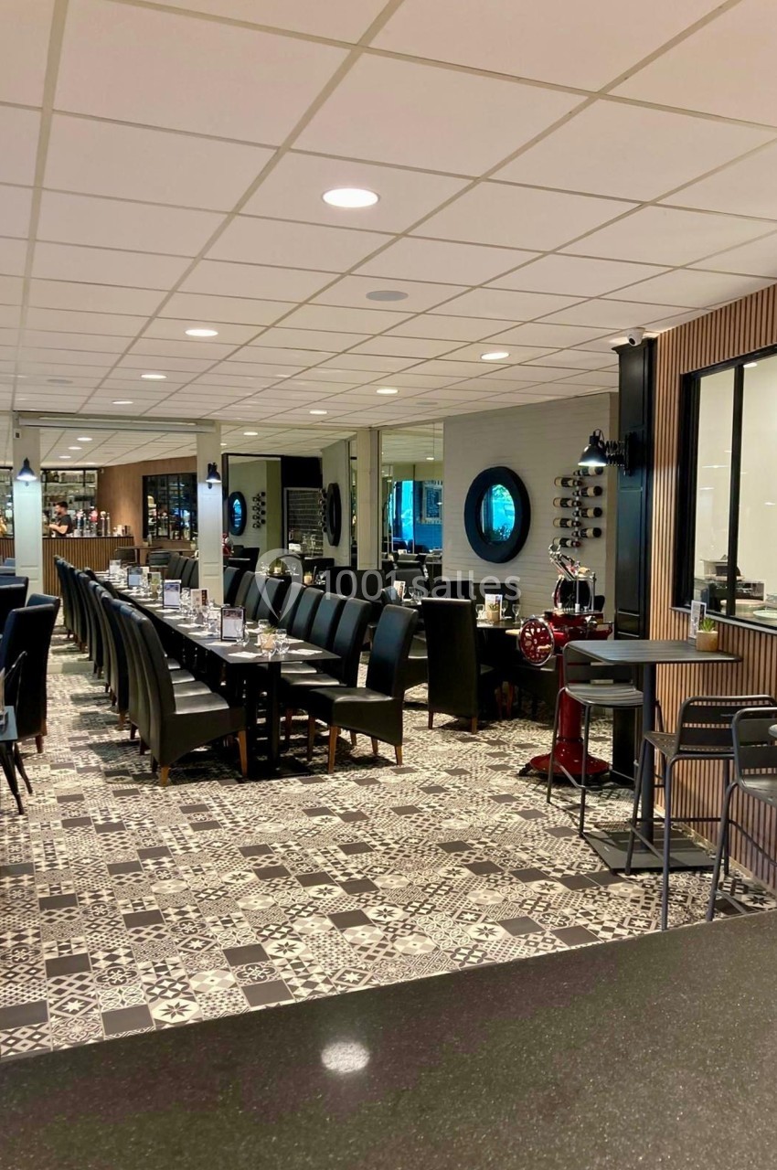 Salle de restaurant moderne avec tables alignées, chaises noires, sol à motifs et ambiance lumineuse.