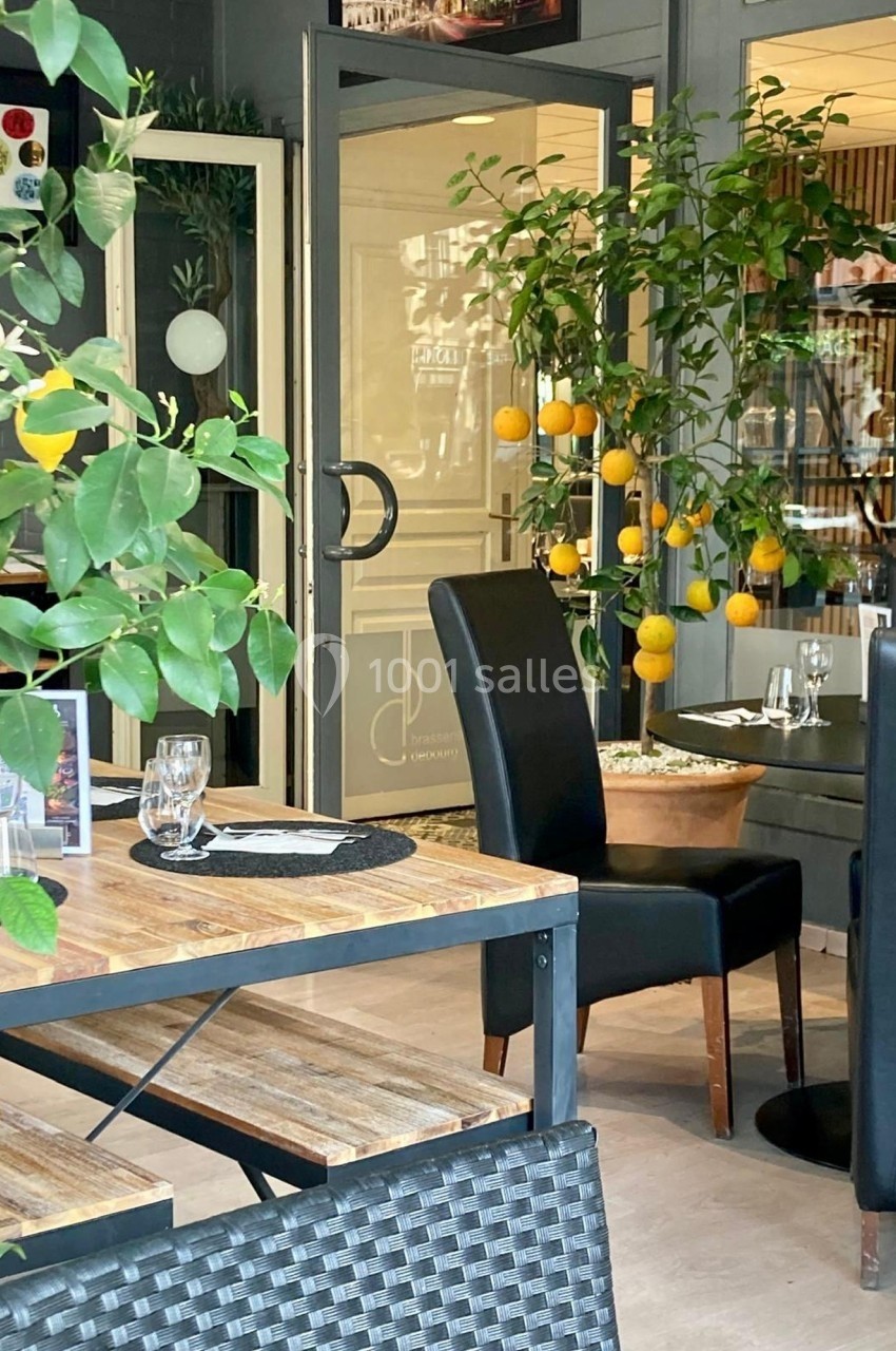 Salle de restaurant lumineuse avec tables en bois, chaises noires et plantes décoratives portant des citrons.