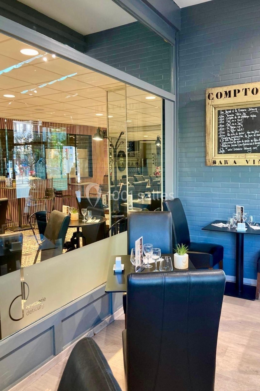 Salle de restaurant moderne avec tables dressées, baies vitrées et ardoise affichant une carte de vins.