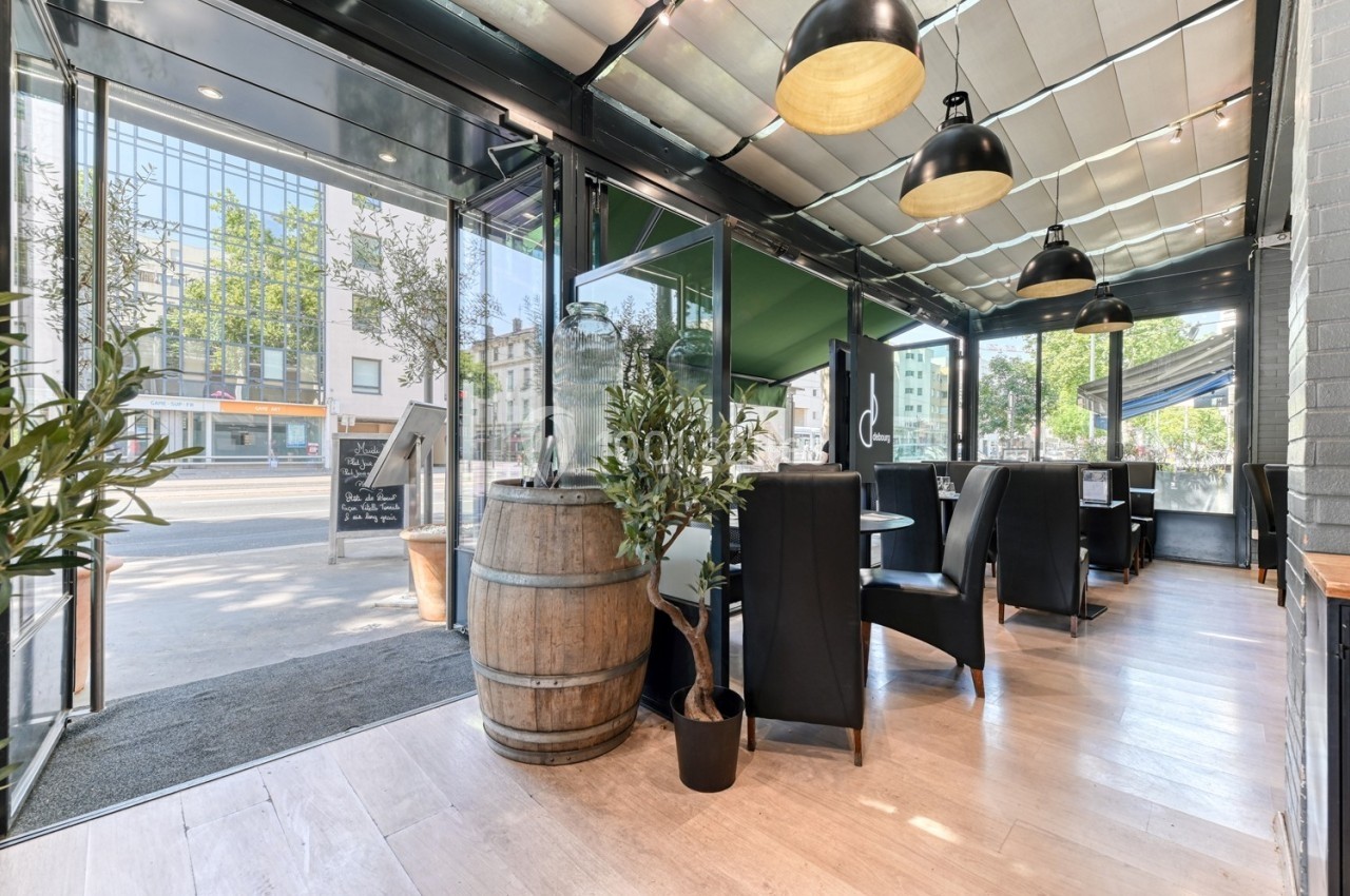 Salle de restaurant lumineuse avec grandes baies vitrées, mobilier moderne et tonneau décoratif en bois.