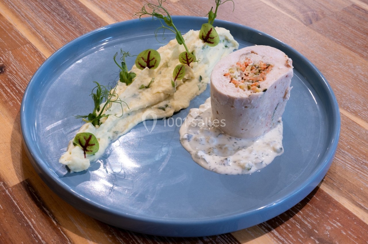 Roulé de volaille farci, purée décorée de micro-pousses et sauce blanche, présenté sur une assiette bleue.