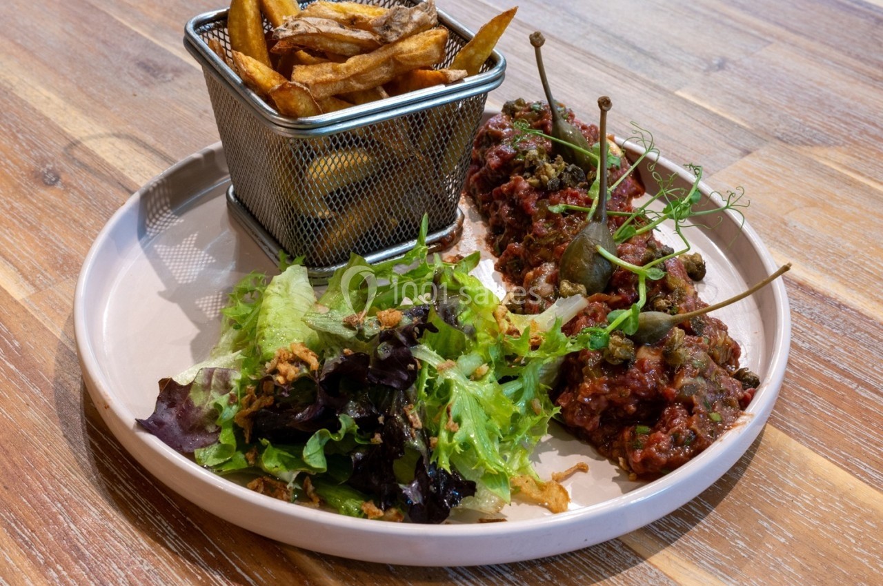 Assiette composée de tartare de viande, salade verte et frites servies dans un petit panier métallique.