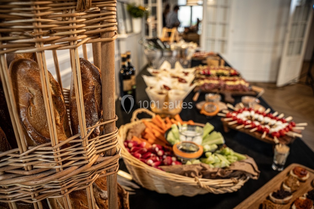 Buffet avec paniers de pain, légumes frais, brochettes et autres plats disposés sur une table dans un cadre intérieur.