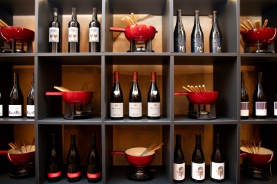 Miniature fondue Fondue au fromage dans un caquelon rouge avec des morceaux de pain trempés, accompagnée de vin et de cornichons.