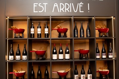 Fondue au fromage dans un caquelon rouge, avec du pain trempé sur des fourchettes, accompagnée de vin et de cornichons.