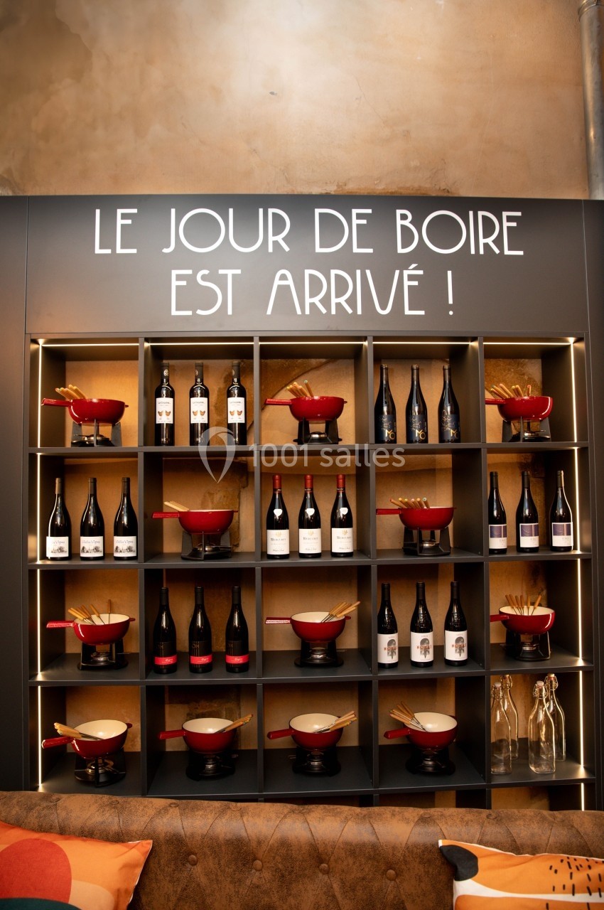 Étagère murale avec bouteilles de vin, caquelons rouges et baguettes, sous une inscription humoristique.