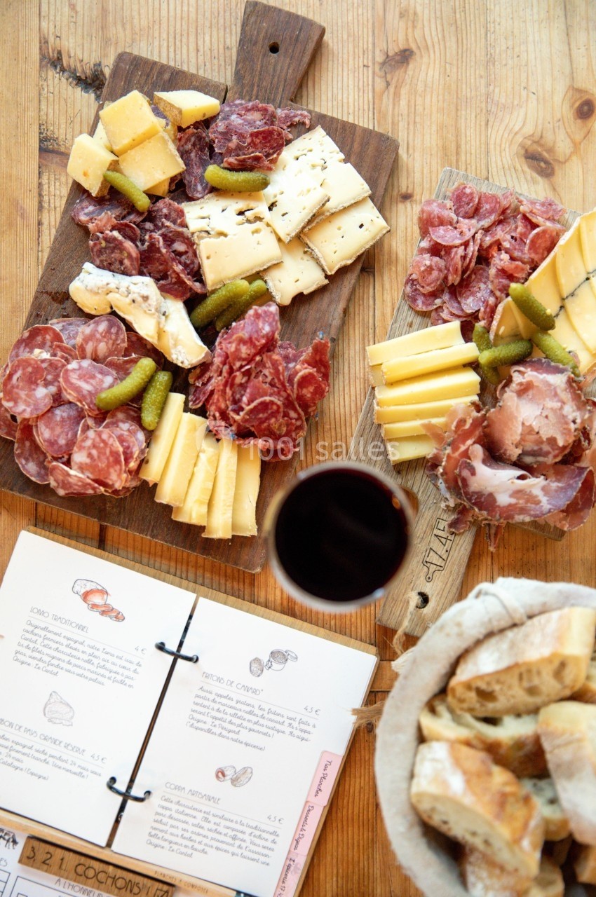 Plateaux de charcuterie et fromages avec cornichons, verre de vin rouge, pain et menu sur une table en bois.