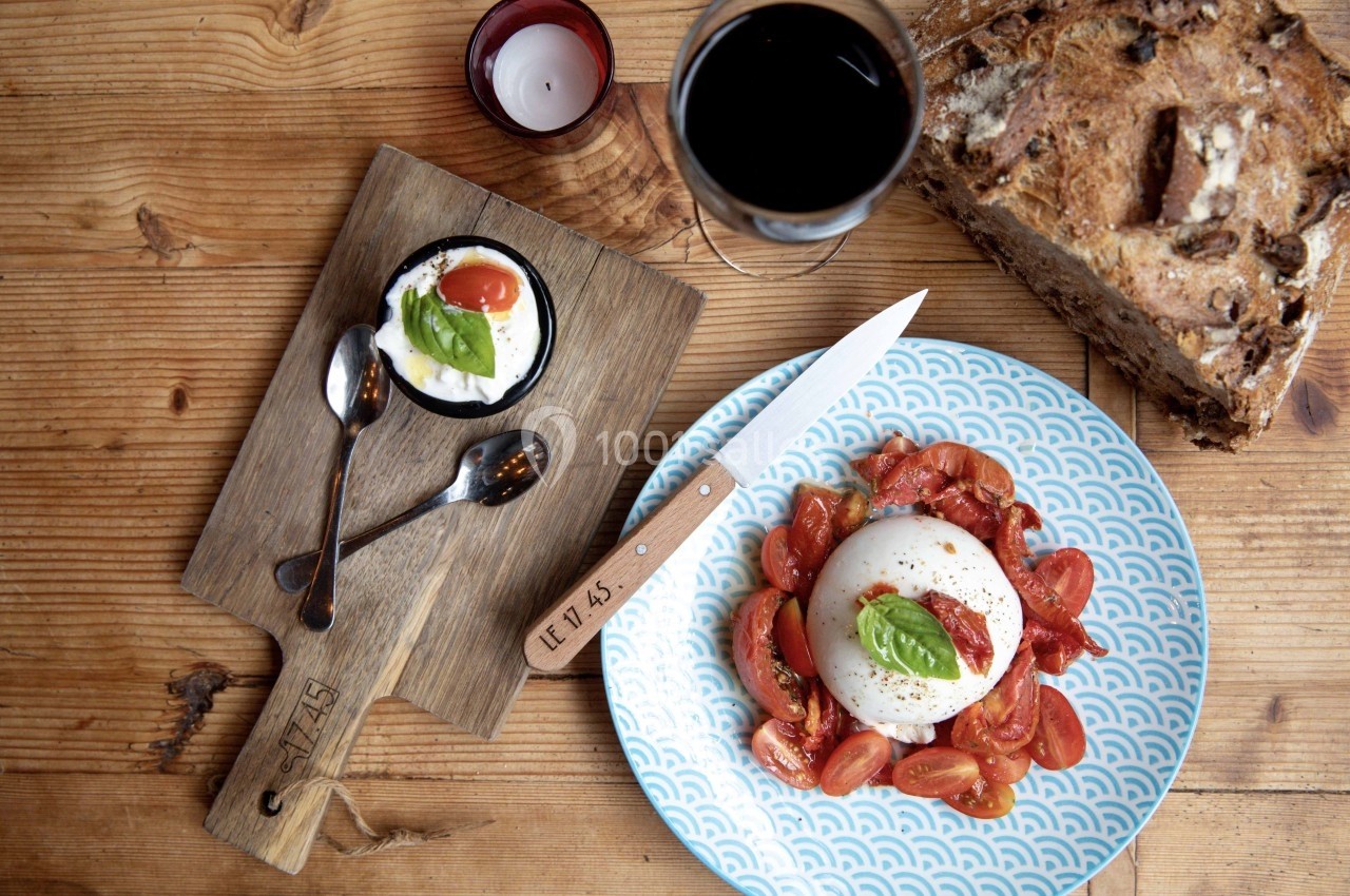 Assiette de burrata avec tomates cerises et basilic, accompagnée de pain, verre de vin et dessert sur une table en bois.
