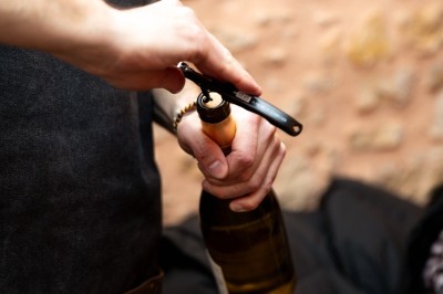 Fondue au fromage dans un caquelon rouge, avec du pain trempé sur des fourchettes, accompagnée de vin et de cornichons.