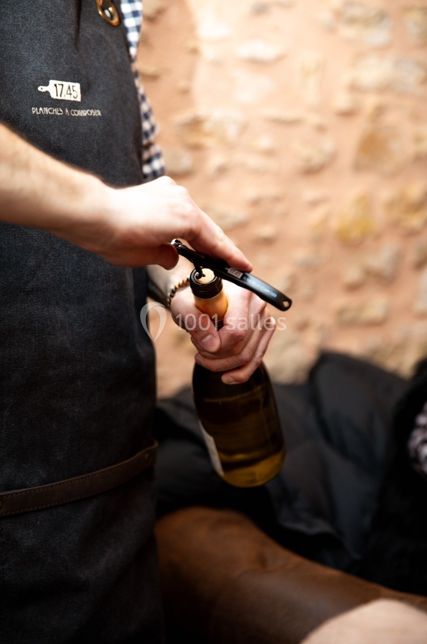 Un serveur ouvre une bouteille de vin à l'aide d'un tire-bouchon dans un cadre intérieur avec un mur en pierre.