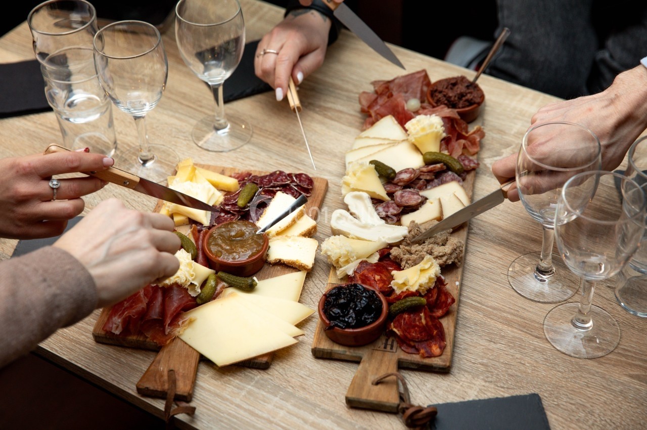 Planche de charcuterie et fromages variés partagée par plusieurs personnes autour d'une table en bois.