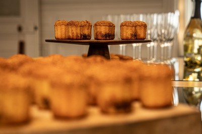 Petits gâteaux dorés disposés sur un présentoir en bois, avec des verres et une bouteille en arrière-plan flou.