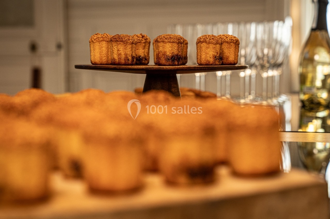 Petits gâteaux dorés disposés sur un présentoir en bois, avec des verres et une bouteille en arrière-plan flou.