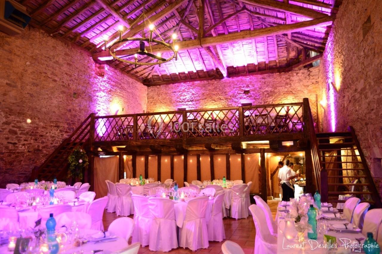 Salle de réception en pierre avec plafond en bois, éclairage violet et tables dressées pour un événement.