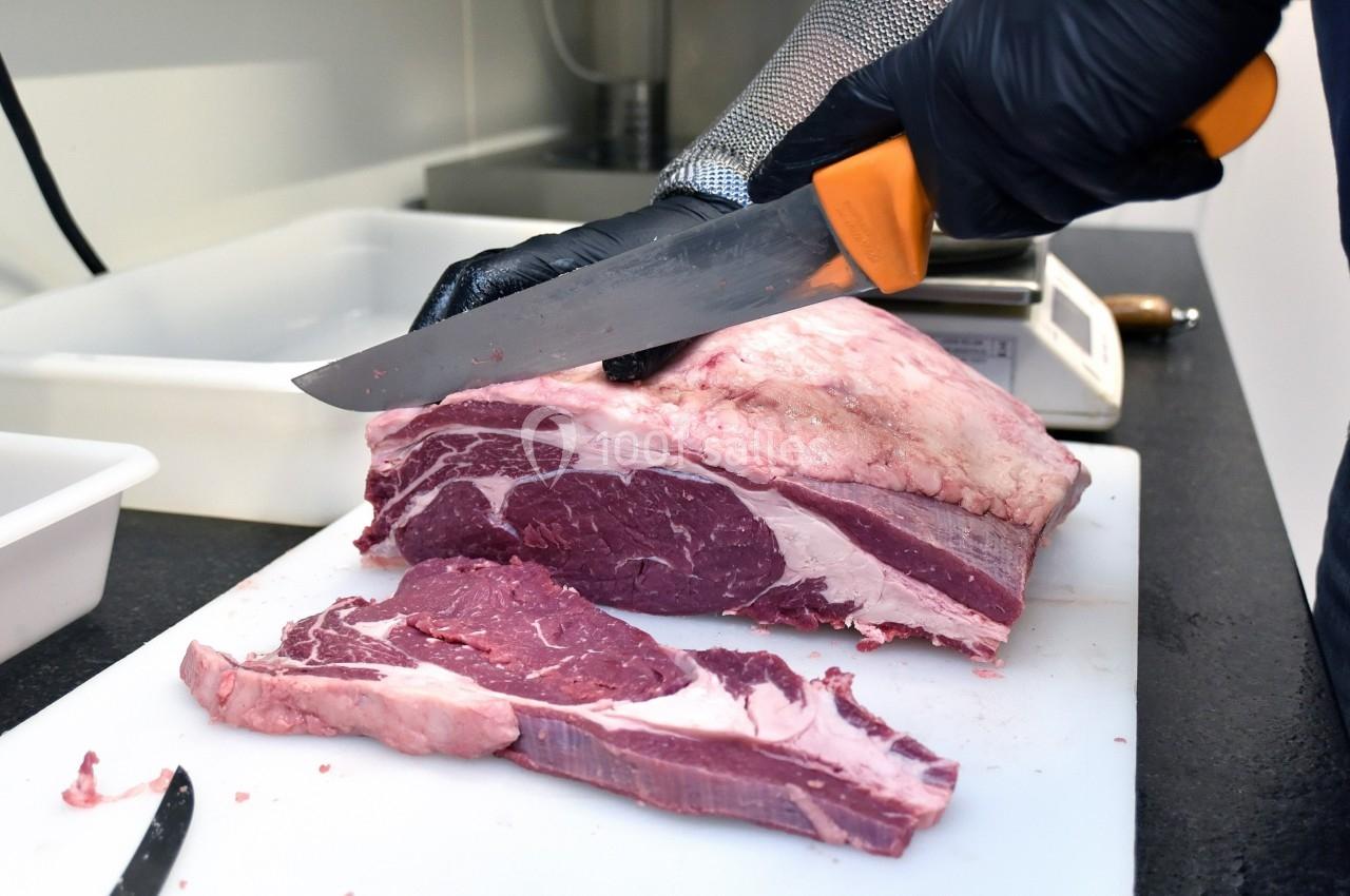 Un boucher découpe un morceau de viande rouge sur une planche blanche avec un couteau.