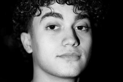 Voiture sportive bleue stationnée sur une place pavée devant un monument en bronze et des bâtiments historiques.