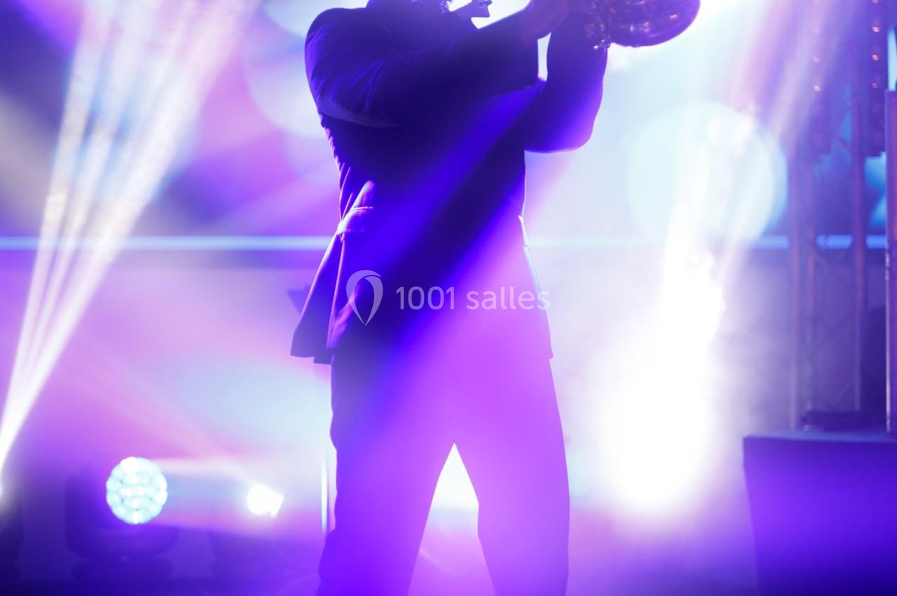 Un musicien joue du saxophone sur scène, éclairé par des projecteurs et des lumières colorées en arrière-plan.