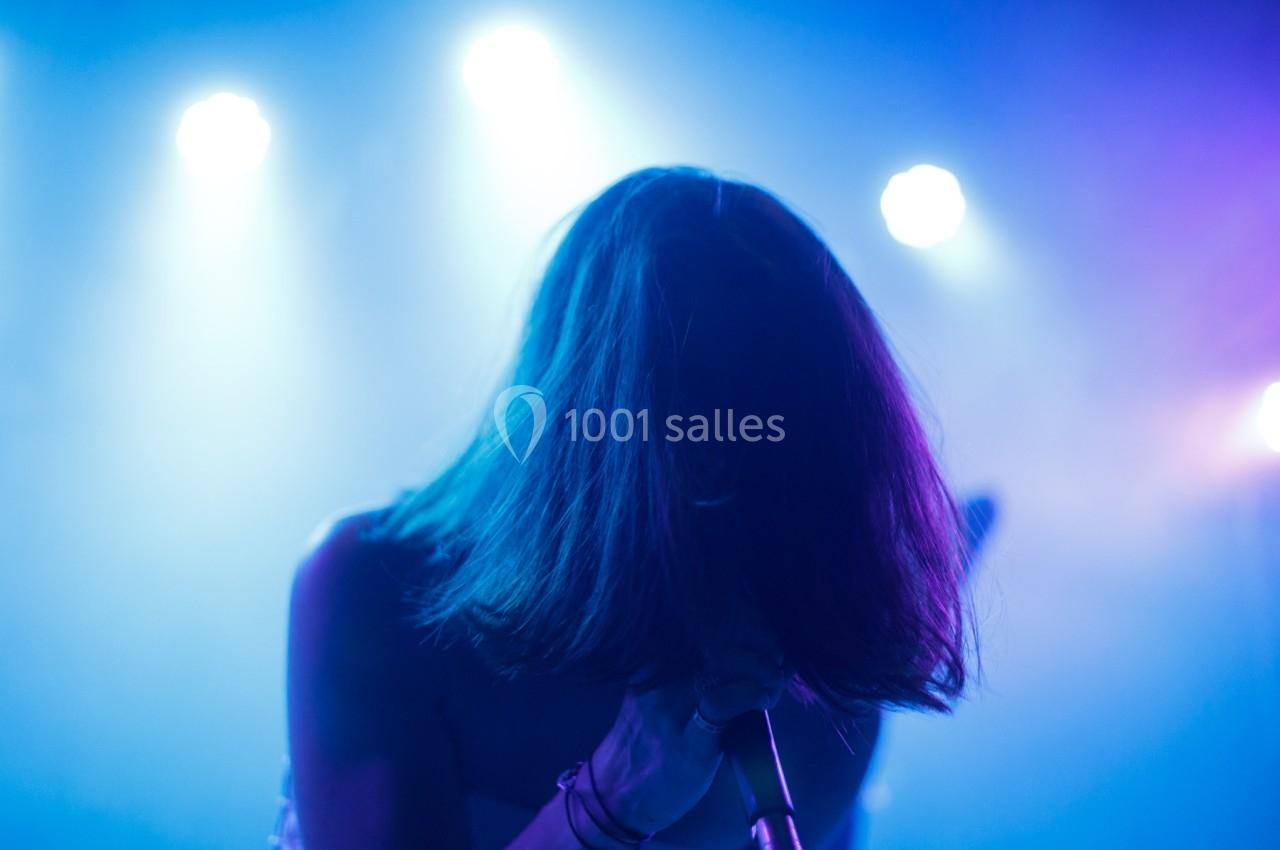 Personne chantant sur scène, éclairée par des lumières bleues et violettes dans une ambiance de concert.