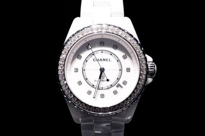 Femme assise sur un banc en extérieur, portant un sweat noir, avec un ciel bleu et des bâtiments en arrière-plan.