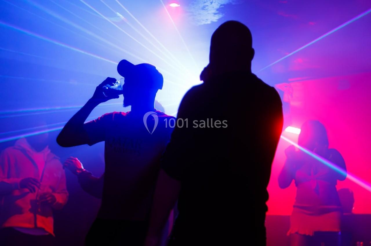 Personnes dans une ambiance de boîte de nuit avec éclairages colorés et effets de lumière.