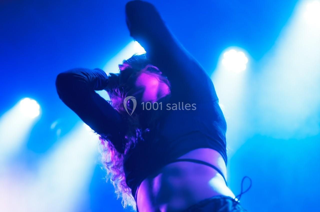 Personne dansant sous des lumières bleues et violettes, bras levés, dans une ambiance de spectacle ou de fête.