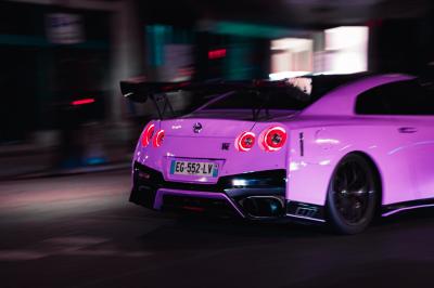 Femme assise sur un banc en extérieur, portant un sweat noir, avec un ciel bleu et des bâtiments en arrière-plan.