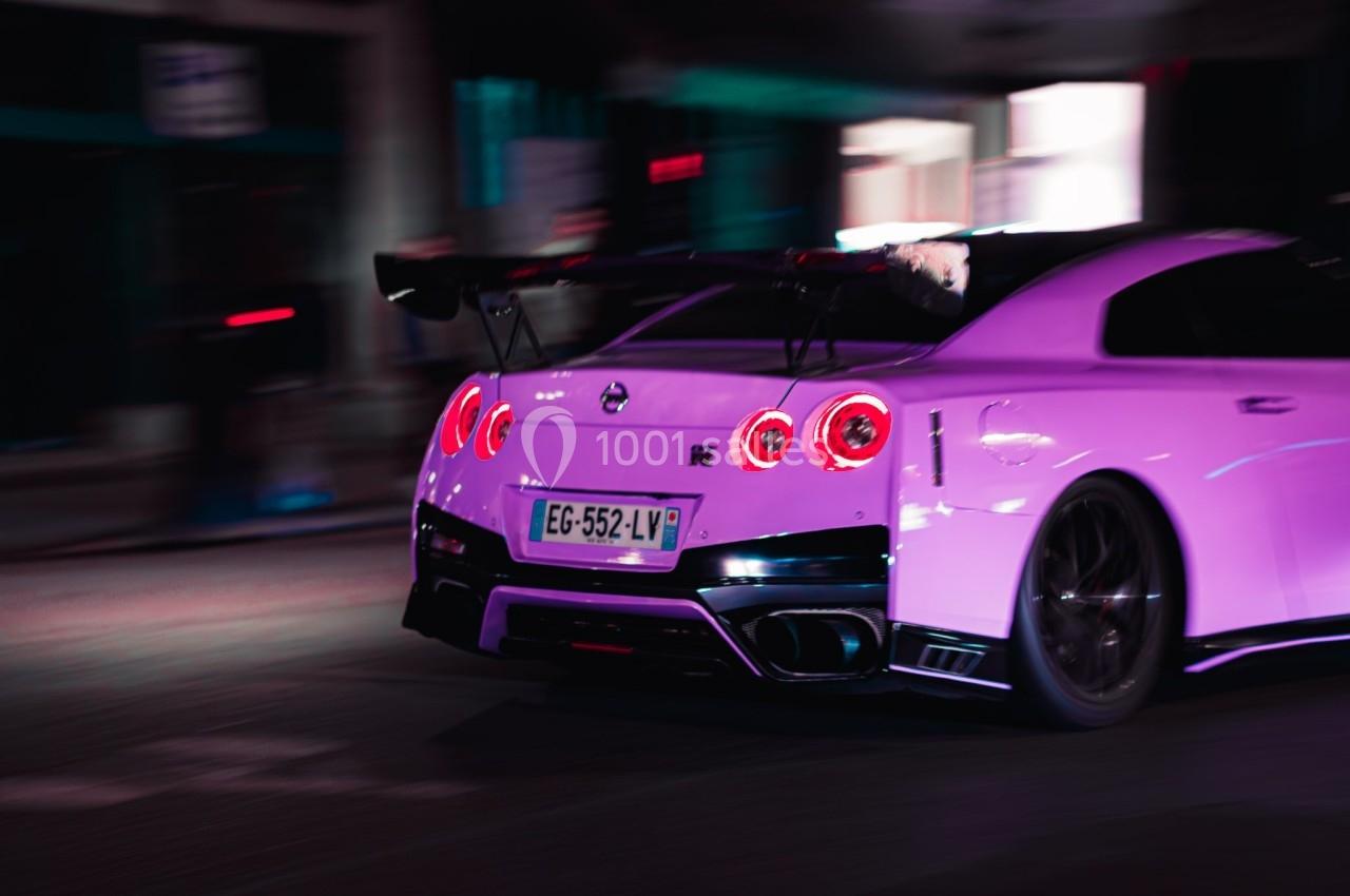 Voiture de sport blanche roulant rapidement dans une rue éclairée par des lumières urbaines.