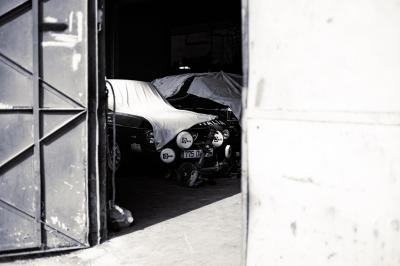 Femme assise sur un banc en extérieur, portant un sweat noir, avec un ciel bleu et des bâtiments en arrière-plan.