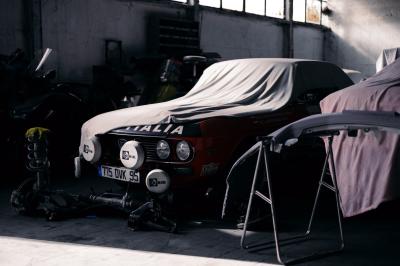 Femme assise sur un banc en extérieur, portant un sweat noir, avec un ciel bleu et des bâtiments en arrière-plan.