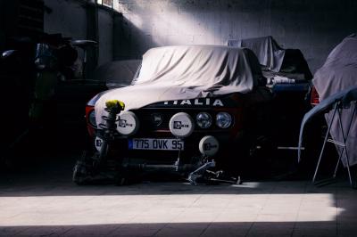 Femme assise sur un banc en extérieur, portant un sweat noir, avec un ciel bleu et des bâtiments en arrière-plan.