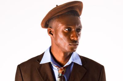 Femme assise sur un banc en extérieur, portant un sweat noir, avec un ciel bleu et des bâtiments en arrière-plan.