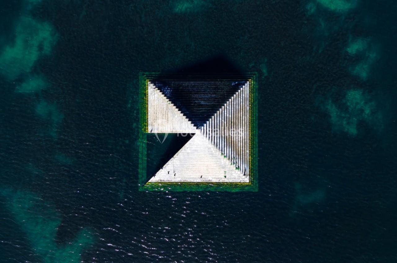 Vue aérienne d'une structure géométrique flottante sur une étendue d'eau sombre avec des reflets et des nuances.