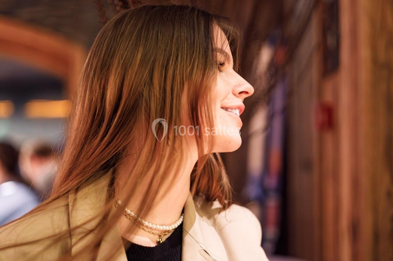 Femme aux cheveux longs souriant de profil dans un intérieur chaleureux avec un éclairage tamisé.
