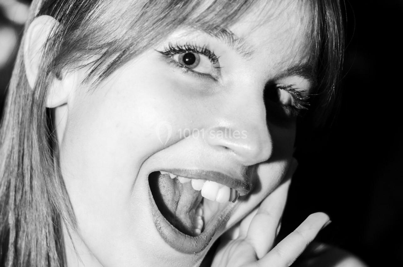 Femme souriante en gros plan, bouche ouverte, éclairée par une lumière contrastée en noir et blanc.