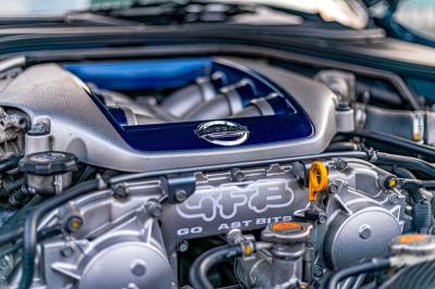 Femme assise sur un banc en extérieur, portant un sweat noir, avec un ciel bleu et des bâtiments en arrière-plan.