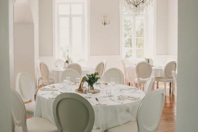 Miniature Location salle Tréflévénez (Finistère) - Château de Kérézellec #2 Un couple de mariés marche vers un château en pierre avec des volets blancs, entouré de quelques invités.