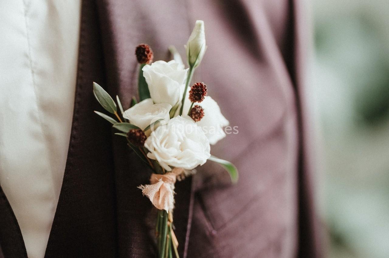 Costume violet avec une boutonnière composée de fleurs blanches et de petites baies rouges.