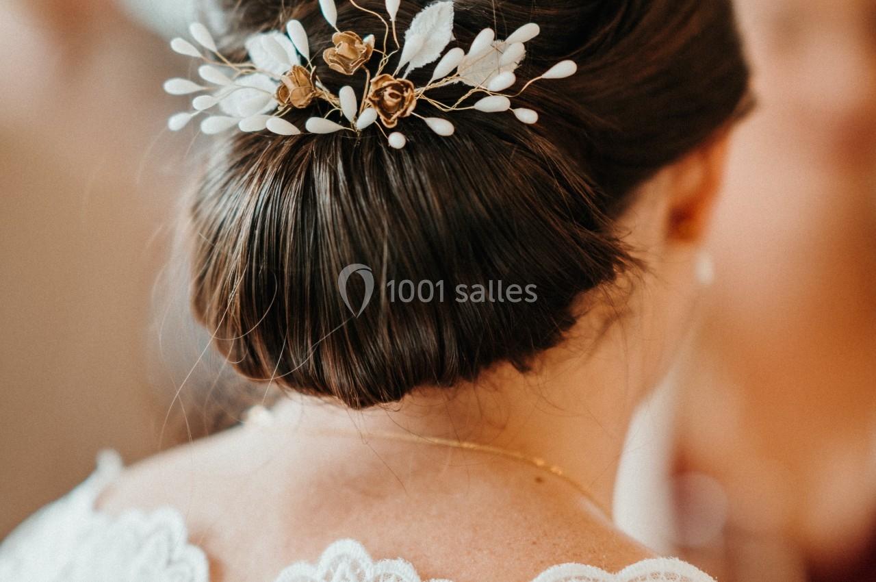 Chignon élégant orné d'une barrette florale avec des détails dorés et blancs, vu de dos.