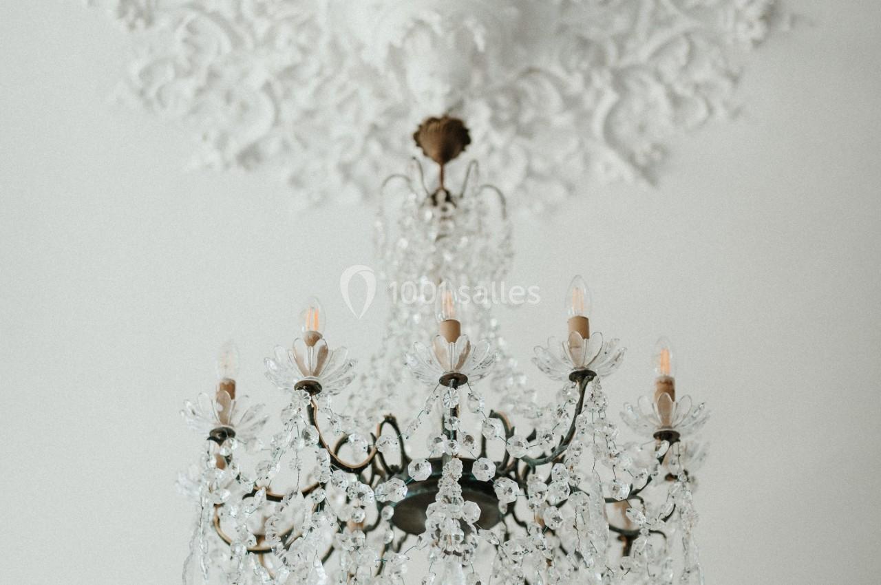 Lustre en cristal suspendu à un plafond orné de moulures blanches détaillées.