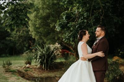 Miniature Location salle Tréflévénez (Finistère) - Château de Kérézellec #12 Un couple de mariés marche vers un château en pierre avec des volets blancs, entouré de quelques invités.