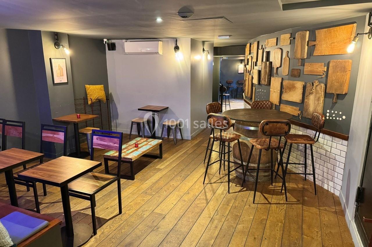 Salle de restaurant avec parquet en bois, tables et chaises variées, murs décorés de planches en bois.